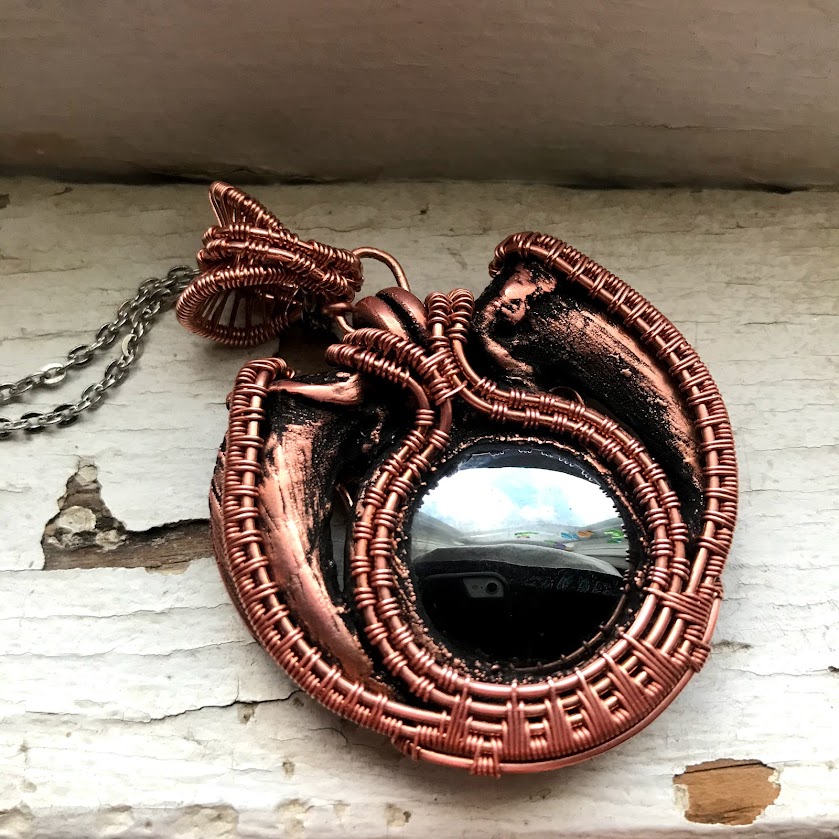 Photo of a necklace pendant. The pendant is comprised of a hematite cabochon surrounded by two electro-formed animal claws.